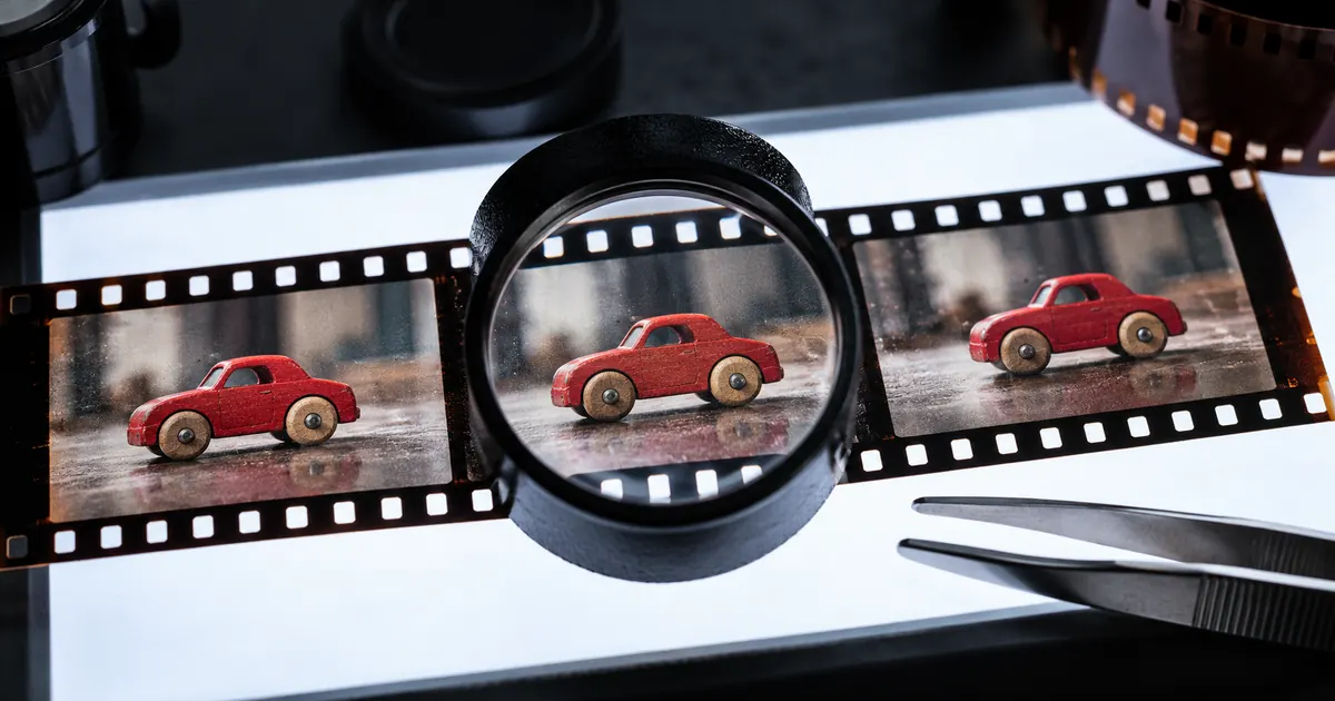 Magnifying loupe inspecting a film strip showing a fictional red wooden toy car.